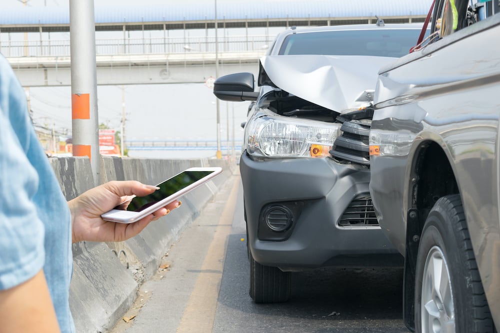 person holding phone next to car crash